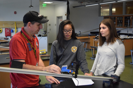 Costa physics teacher, Jon Lewis, demonstrates lab procedures for seniors Carley Resin and Lulu Tojo in room 237 Tuesday during 4th period.  He helped the seniors better understand what their data represented.