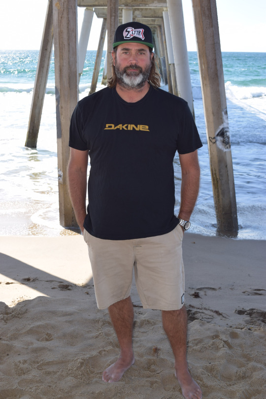 Broza poses underneath the Hermosa Beach pier where he takes his bike, camera, and a cup of coffee every morning to photograph the smooth morning break.