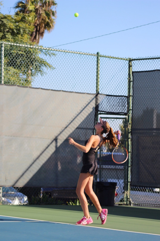 Senior Varsity player Jackie Soliman throws the ball up and positions herself to follow through with an overhead serve.