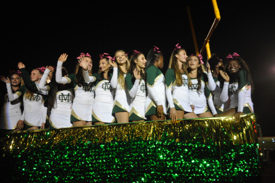 The members of the Mira Costa High School cheer team wave to the crowd as they pass by the bleachers.