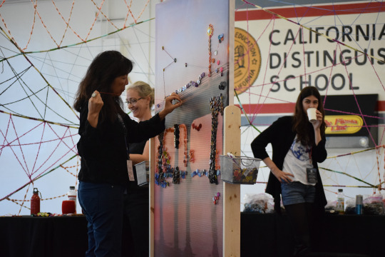 Mrs. Matsui is sticking colorful pins into a board outlining the Manhattan Beach pier.