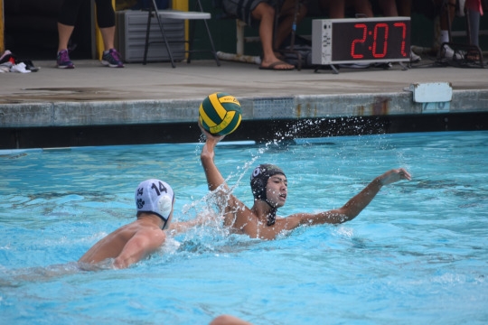 Water polo player makes a pass with strong defense from Loyola player number 14.
