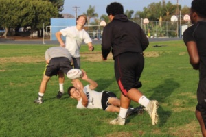 Boys Rugby players perform a tackle-pass drill where one player sets down a ball, another grabs it, and the last tackles the player with the ball.