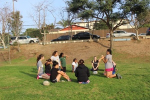 Girls Rugby players huddle with their coach to discuss the team’s strengths, weaknesses, and how to improve in the future.