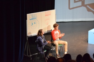 Isabel Gray (left) keeps score for the blue team and Duncan Bardeau (right) keeps score for the red team. The scorekeepers watched and kept score from the side of the lefthand stage.