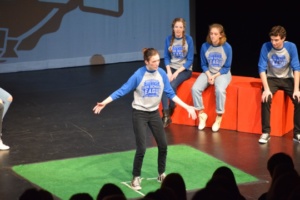 Riley Douglas plays “players on the playing field” for the first game in the match. In this game, players improv in the white taped box about a given subject.