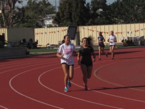 Senior Sara Gustafson (left) and Ashley Werre (right) run around the track after 5th period on Monday. The members of the long distance track team run two laps around the track every day for their warm up. 