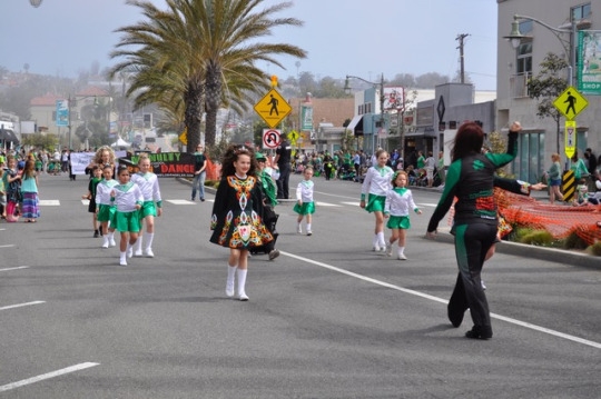 A group of dancers walks in the parade and periodically stops to dance for the  surrounding crowd. This group of dancers was led by their dance teacher as they danced in the parade. 